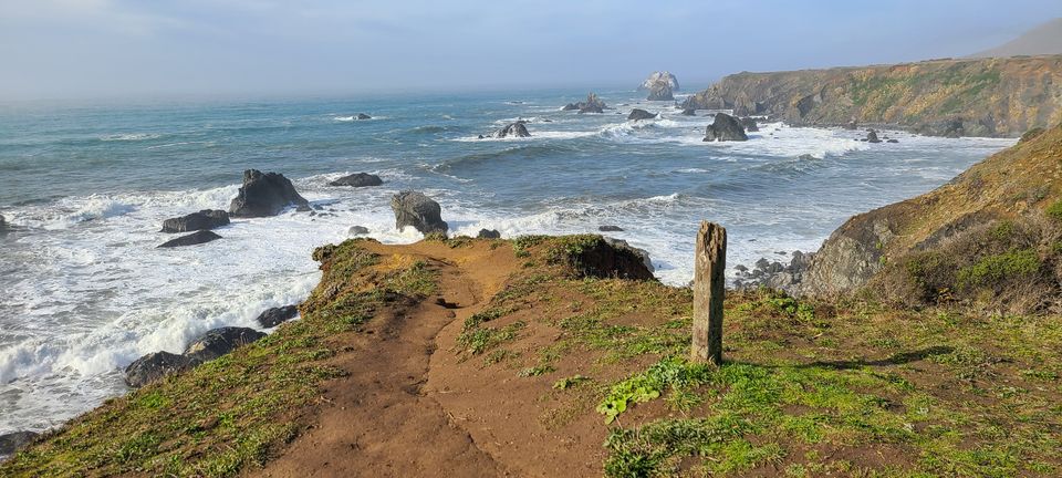 A path ending in a rocky coastline with waves crashing on rocks below the end of the path.